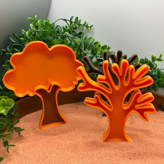 Orange autumn leafy tree filling tray standing in sand beside a matching orange bare branch tree
