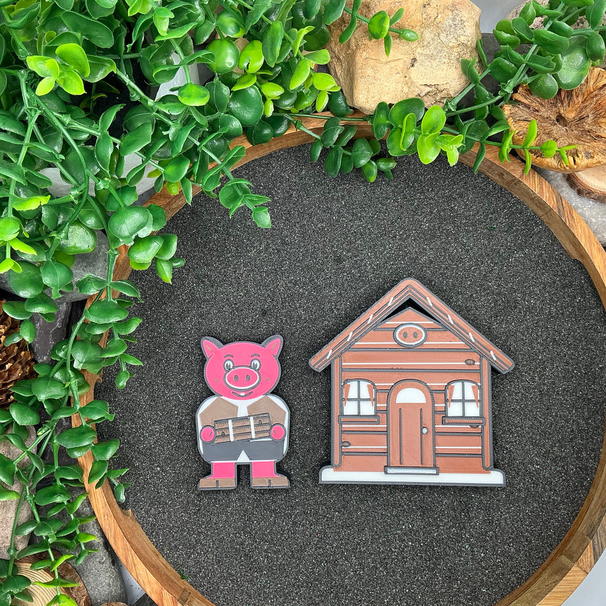Small pig character beside the brown stick house, laid flat in a wooden sand tray