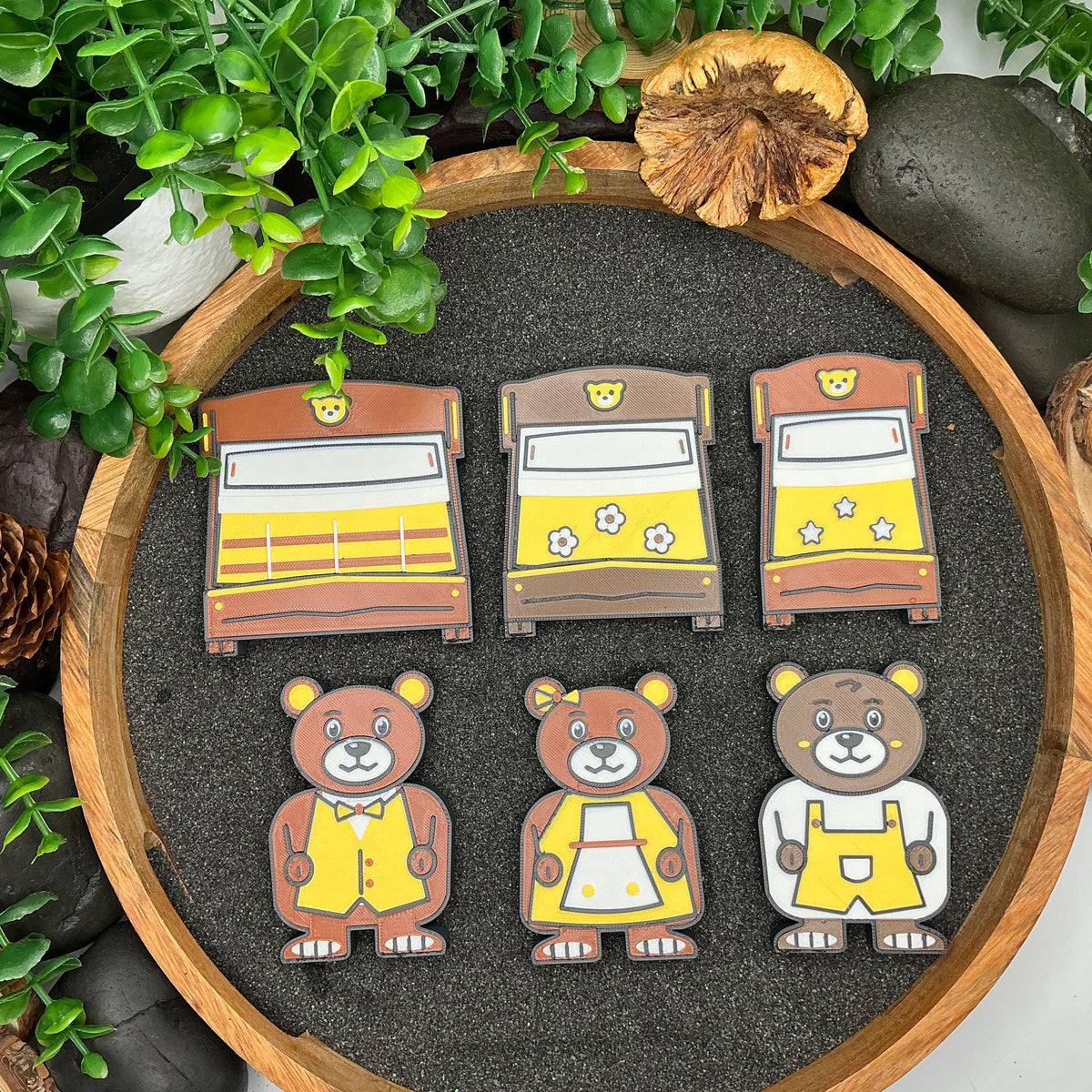 Three bear figures and their striped, flower and star bed pieces laid out in sand
