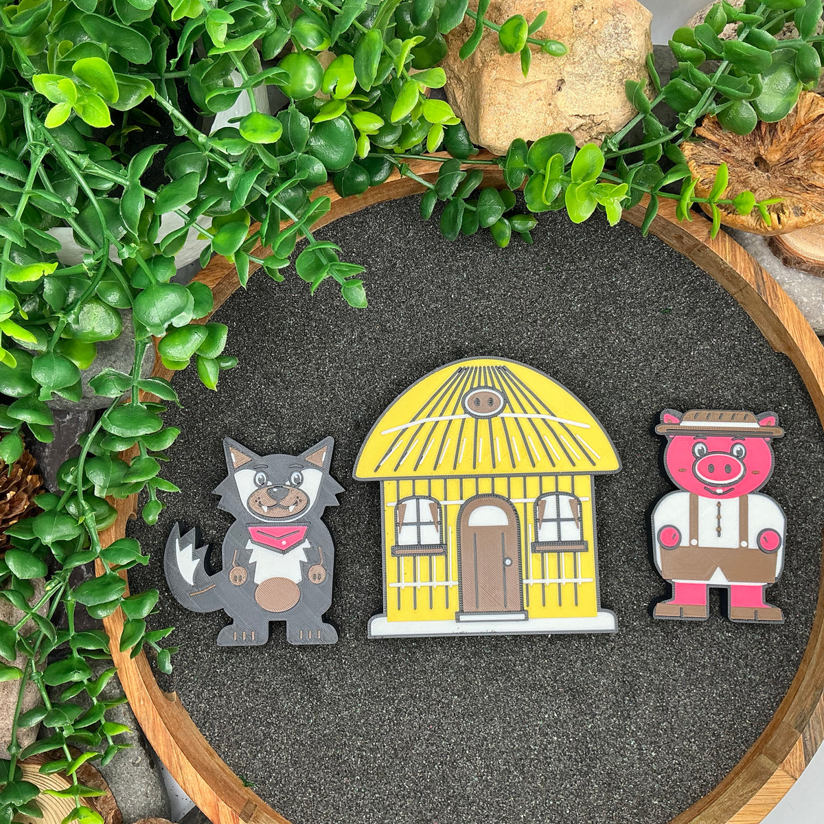 Small wolf and pig figures beside the yellow straw house, laid flat in sand