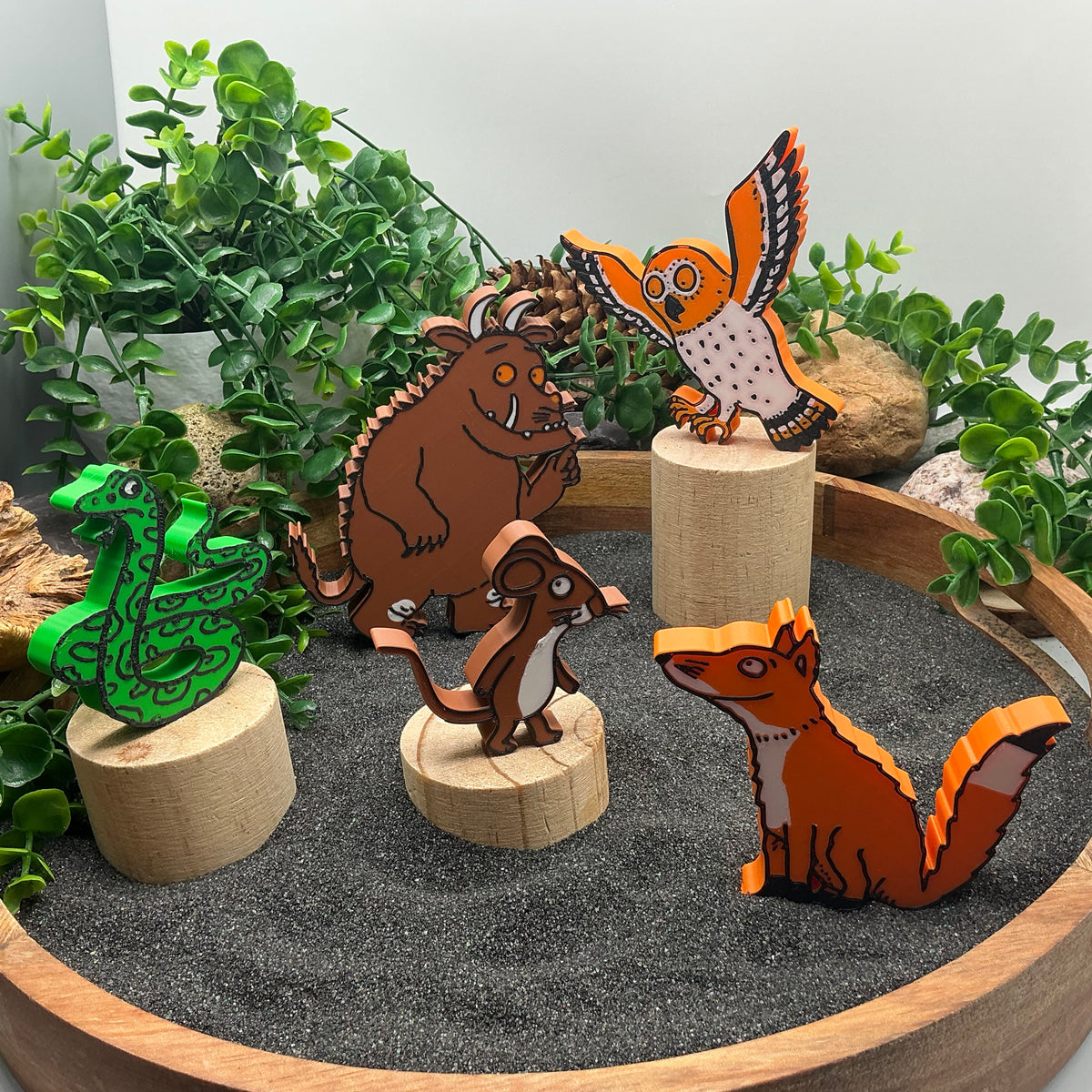 Woodland story characters standing in sand, some on wooden log stands