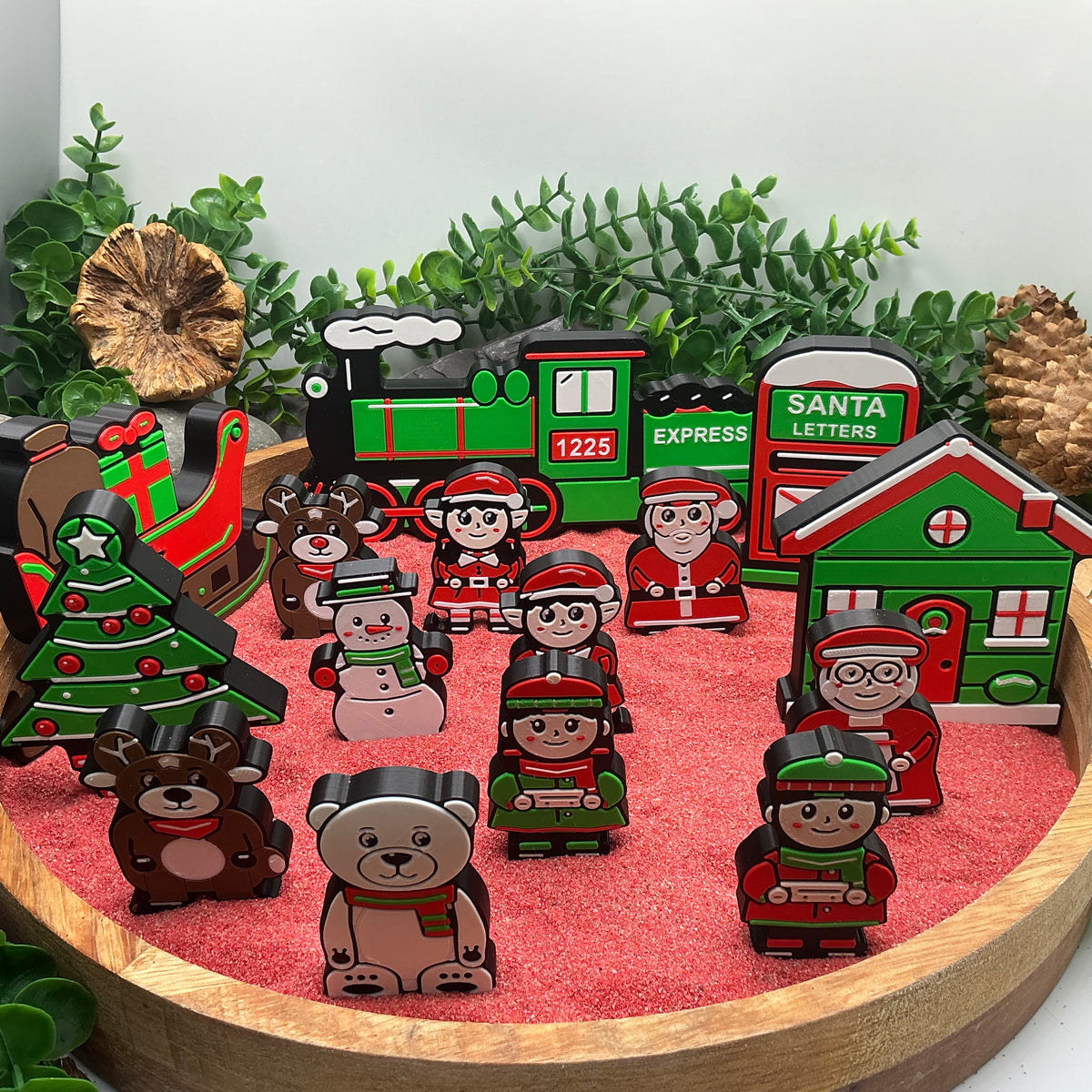 Christmas characters and animals standing with the express train, cottage, sleigh, tree and post box in a red sand tray