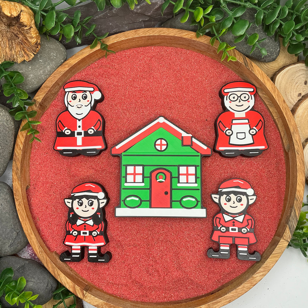Mr Claus, Mrs Claus, boy elf and girl elf arranged around the green Christmas cottage