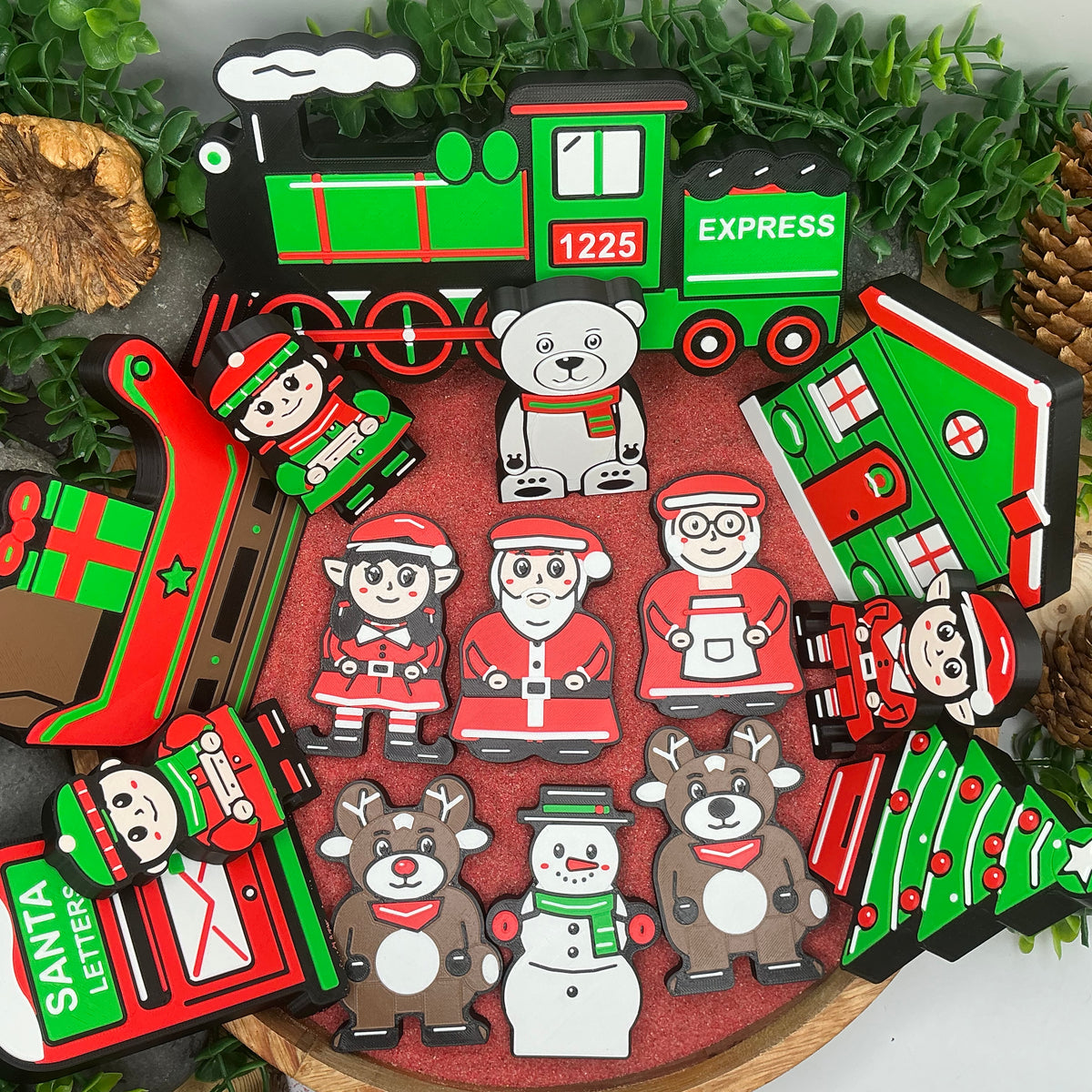 Complete 15-piece Christmas collection laid flat in a wooden tray, with Claus figures, elves, two reindeer, snowman, polar bear, train, passengers, cottage, sleigh, tree and Santa letters post box