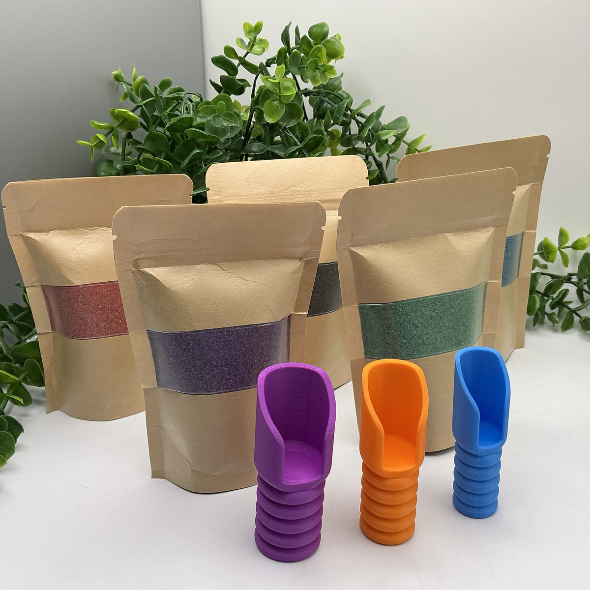 Five pouches of coloured play sand with purple, orange and blue pouring scoops